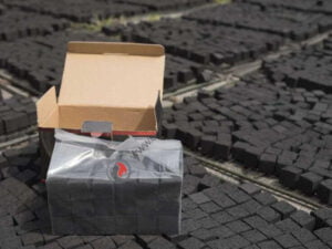 Charcoal briquettes in inner plastic and inner box behind with other briquettes under it.